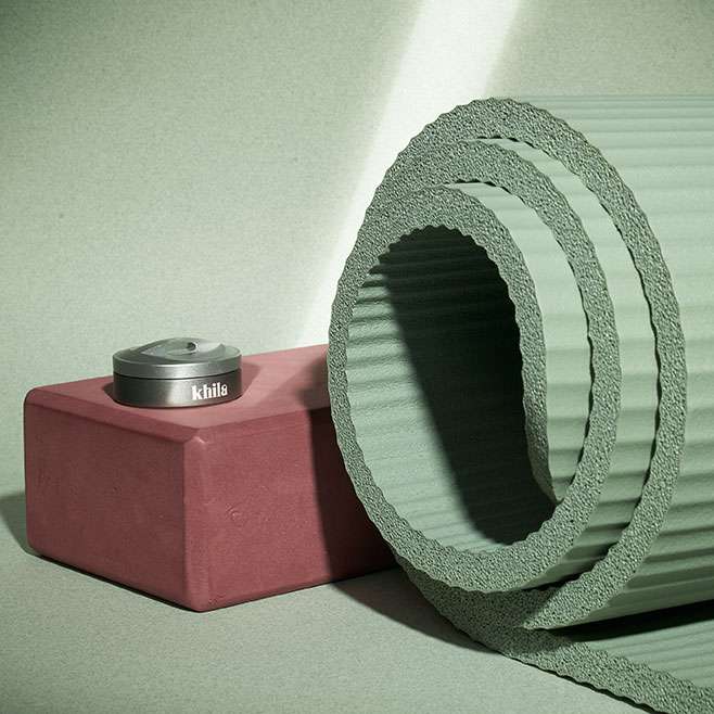 A Khila Life pill organiser placed upon a yoga block. There is a rolled up yoga mat to the side of it.