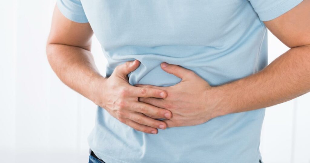 Man in blue t shirt holding stomach in pain from flatulence and intestinal gas